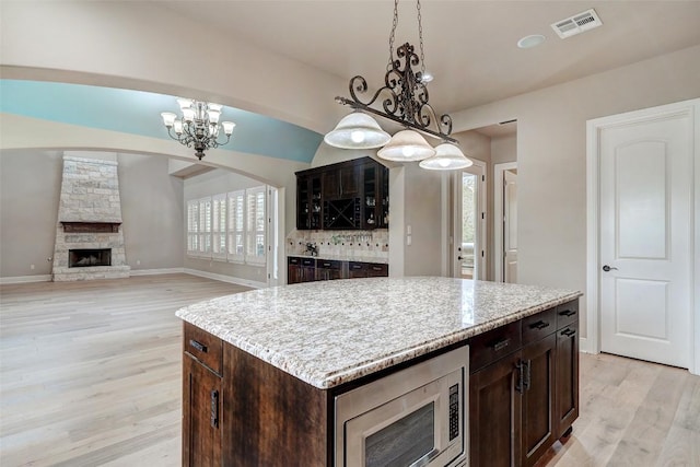 kitchen with visible vents, dark brown cabinets, stainless steel microwave, a chandelier, and light wood finished floors