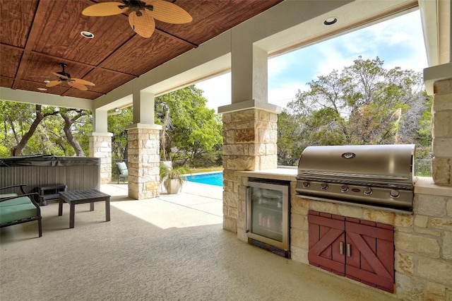 view of patio featuring a hot tub, exterior kitchen, beverage cooler, area for grilling, and a ceiling fan