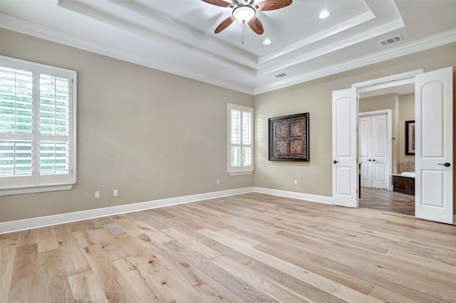 unfurnished bedroom with crown molding, a tray ceiling, light wood-style flooring, and visible vents