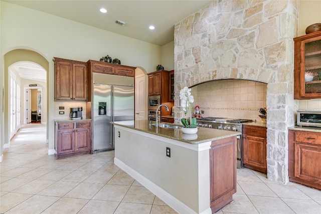 1916 Wimberly Ln, Austin, TX 78735 - kitchen with built in appliances, light tile patterned flooring, arched walkways, a kitchen island with sink, and backsplash