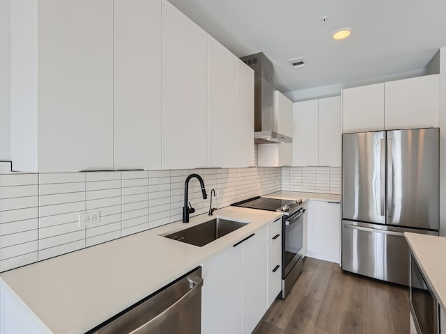 kitchen featuring wall chimney range hood, light countertops, a sink, stainless steel appliances, and white cabinetry
