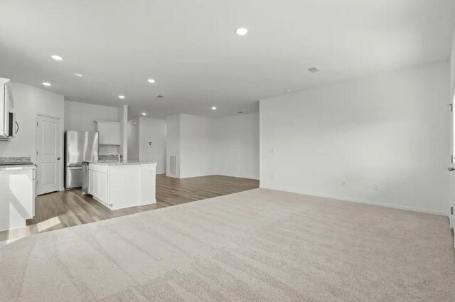 unfurnished living room with a sink, light wood finished floors, recessed lighting, and visible vents