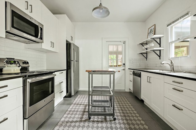 kitchen with open shelves, appliances with stainless steel finishes, dark countertops, a sink, and backsplash