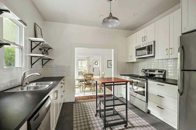kitchen featuring a healthy amount of sunlight, dark countertops, stainless steel appliances, and a sink