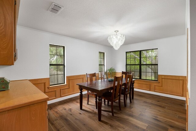 dining area featuring visible vents, ornamental molding, wainscoting, dark wood-type flooring, and a notable chandelier