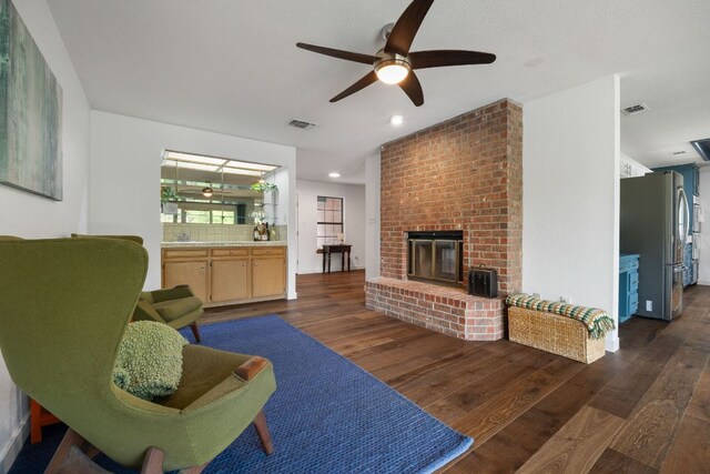 living area featuring visible vents, a ceiling fan, dark wood finished floors, and a brick fireplace
