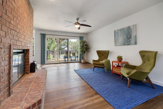 sitting room featuring baseboards, a ceiling fan, a brick fireplace, and wood finished floors