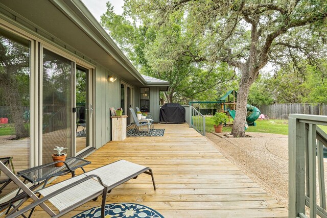 wooden terrace featuring a fenced backyard, a playground, and a grill