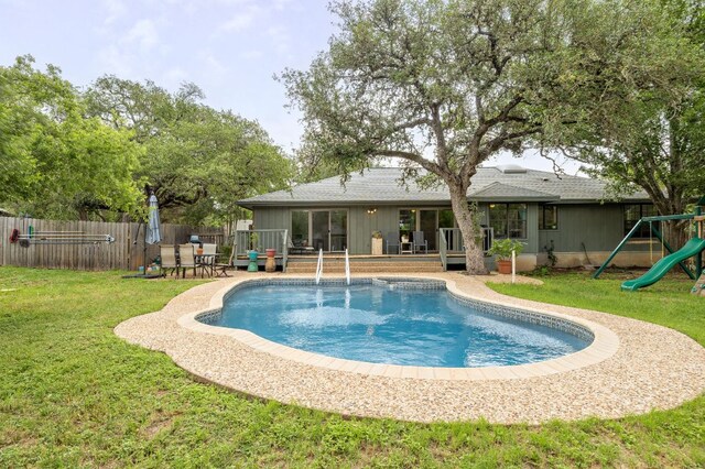 view of pool featuring a lawn, a wooden deck, fence, a fenced in pool, and a playground