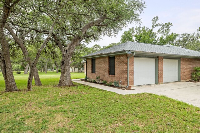 view of home's exterior with roof with shingles, an attached garage, brick siding, concrete driveway, and a yard