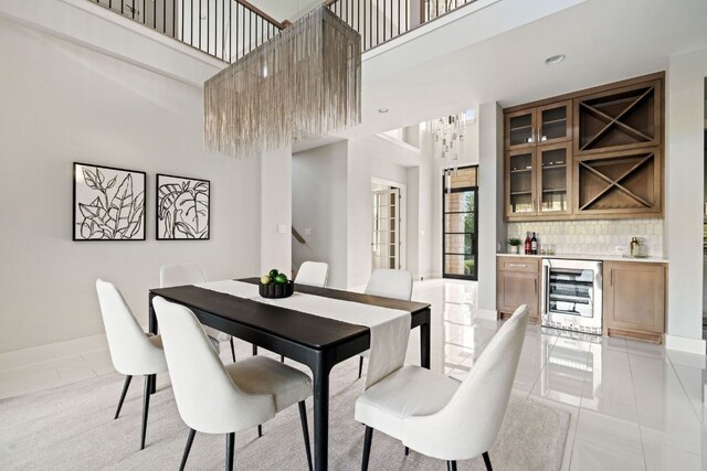 dining space featuring a towering ceiling, baseboards, indoor wet bar, beverage cooler, and light tile patterned flooring
