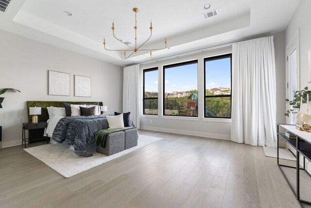 bedroom featuring a tray ceiling, light wood-style floors, a notable chandelier, and visible vents