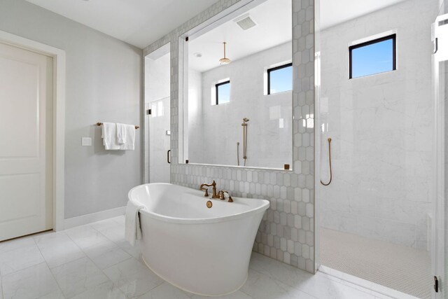 bathroom with a freestanding bath, a wealth of natural light, a tile shower, and marble finish floor