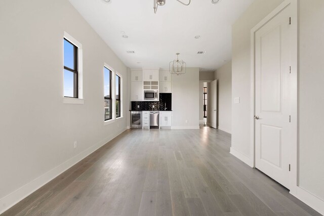 unfurnished living room with baseboards, an inviting chandelier, wood finished floors, and visible vents