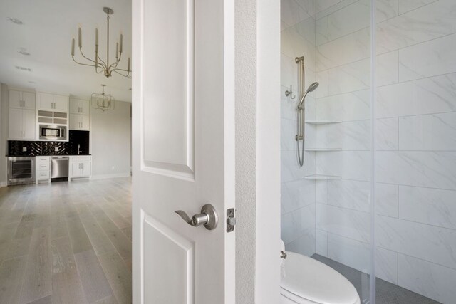 bathroom with an inviting chandelier, wood finished floors, toilet, beverage cooler, and a shower stall