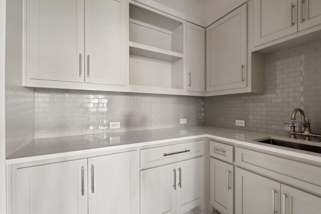 kitchen with decorative backsplash, open shelves, a sink, light countertops, and white cabinetry