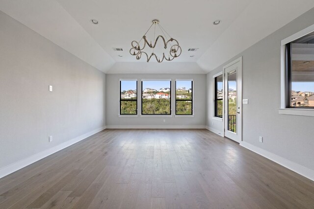interior space with a healthy amount of sunlight, vaulted ceiling, wood finished floors, and a chandelier