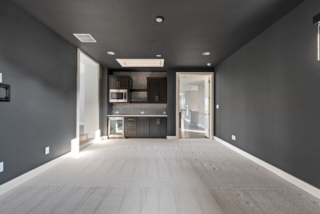 unfurnished living room featuring baseboards, light carpet, bar, and beverage cooler