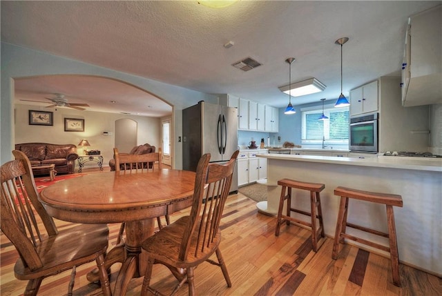 dining area featuring light wood-style floors, arched walkways, a ceiling fan, and visible vents