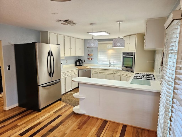 kitchen with a peninsula, light countertops, a sink, light wood finished floors, and stainless steel appliances
