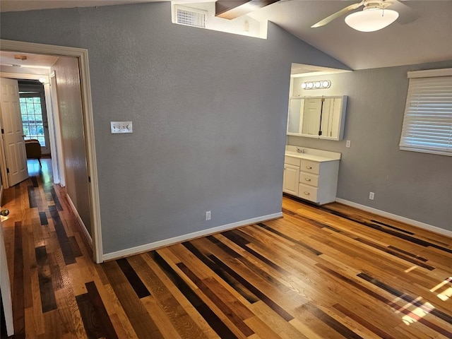unfurnished bedroom with visible vents, wood finished floors, baseboards, lofted ceiling, and a textured wall