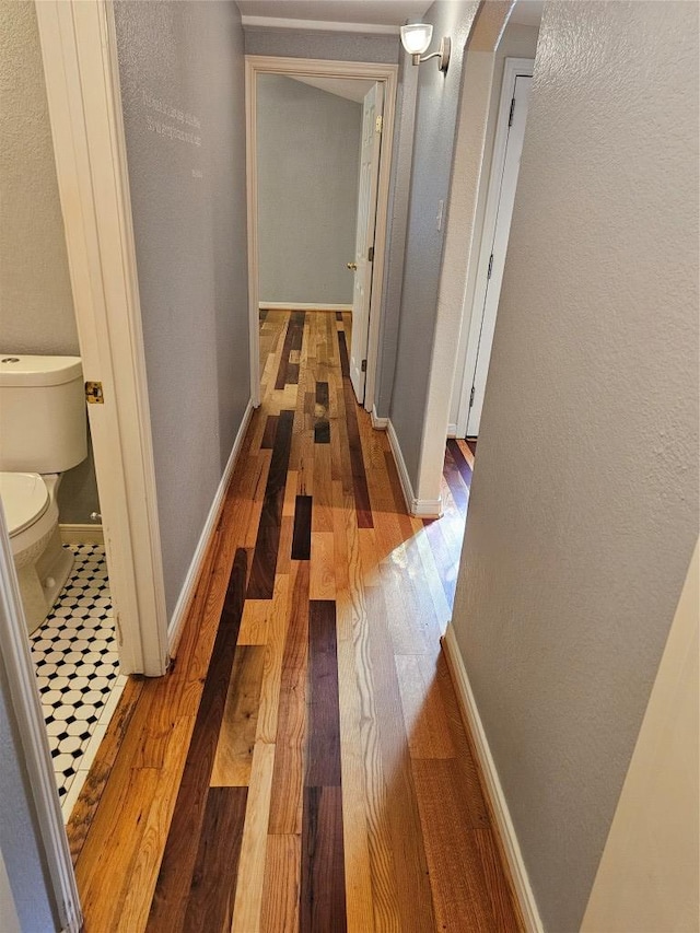 hallway with arched walkways, baseboards, a textured wall, and wood finished floors