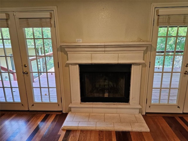 room details featuring a fireplace with raised hearth, french doors, and wood finished floors