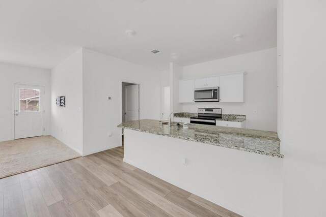kitchen featuring appliances with stainless steel finishes, light stone countertops, a sink, white cabinets, and light wood finished floors