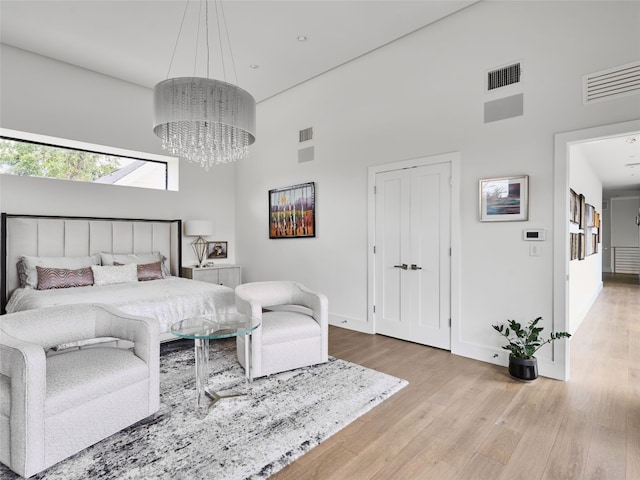 bedroom featuring light wood-style floors, baseboards, visible vents, and a towering ceiling