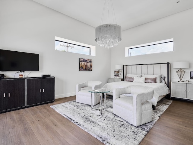 bedroom with an inviting chandelier, baseboards, a towering ceiling, and wood finished floors