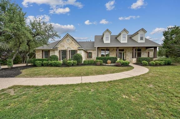 new england style home featuring a front yard, stone siding, and covered porch