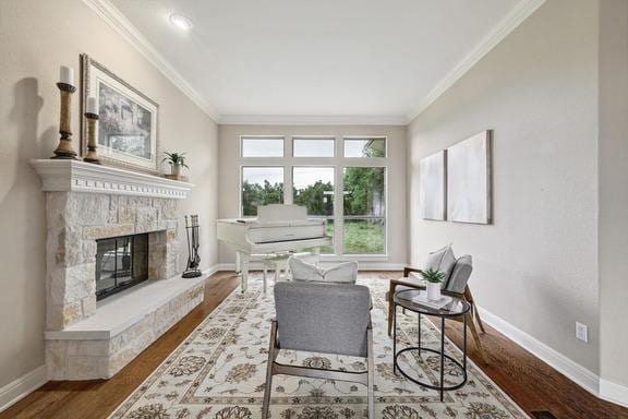 living area featuring crown molding, baseboards, a stone fireplace, and wood finished floors