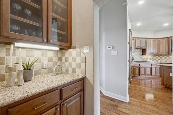 bar featuring arched walkways, light wood-style floors, baseboards, and tasteful backsplash
