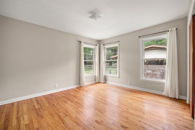 empty room featuring light wood-style floors, baseboards, and a healthy amount of sunlight
