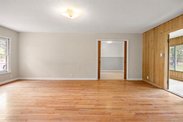 empty room with wood walls, plenty of natural light, and light wood finished floors