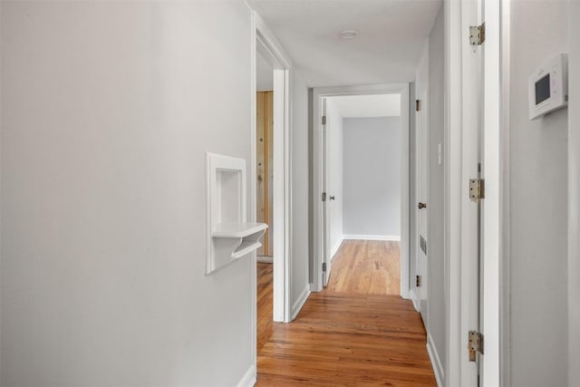 corridor with baseboards and light wood finished floors