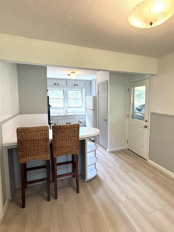 dining room featuring baseboards, a textured ceiling, and light wood-style flooring