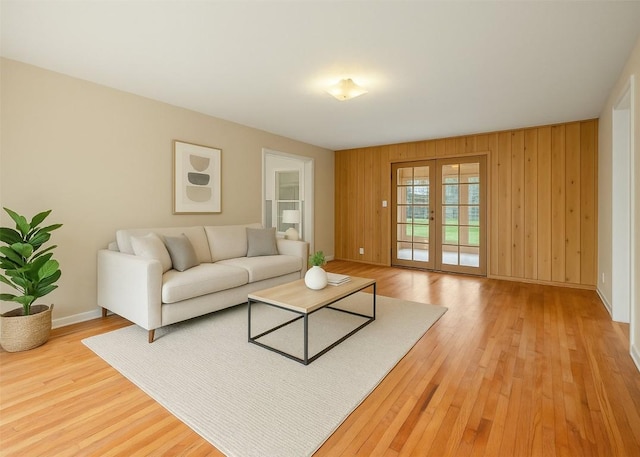 living area with light wood-type flooring, wood walls, baseboards, and french doors