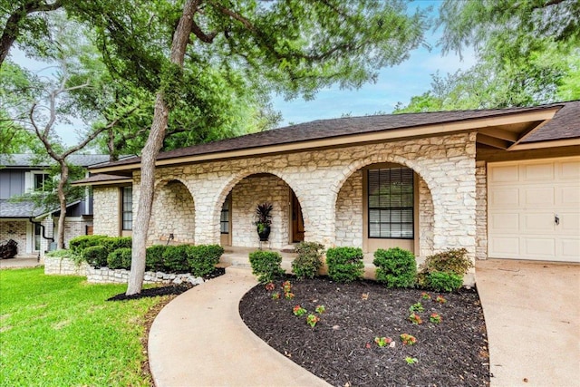 view of front of property featuring covered porch, a front lawn, concrete driveway, an attached garage, and stone siding
