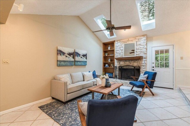 living room with light tile patterned flooring, a stone fireplace, baseboards, high vaulted ceiling, and a skylight