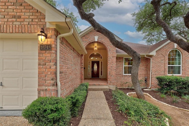 entrance to property featuring an attached garage and brick siding