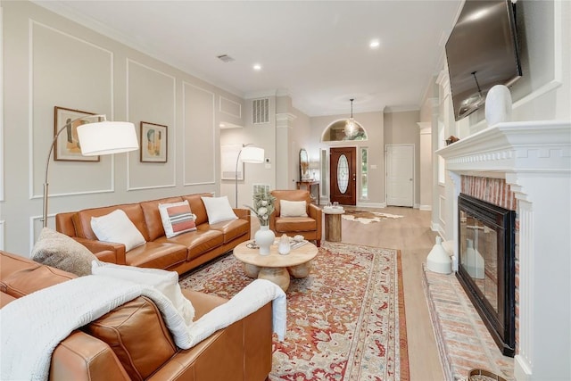 living room with crown molding, visible vents, a decorative wall, recessed lighting, and light wood-type flooring