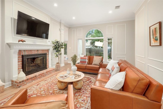 living area with visible vents, crown molding, a brick fireplace, a decorative wall, and wood finished floors