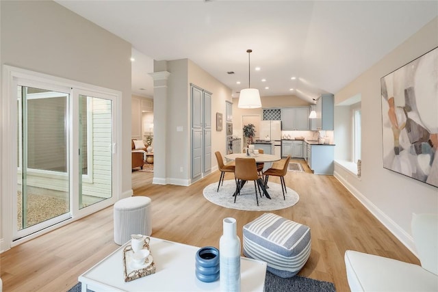 dining area featuring baseboards, vaulted ceiling, a healthy amount of sunlight, and light wood-style floors