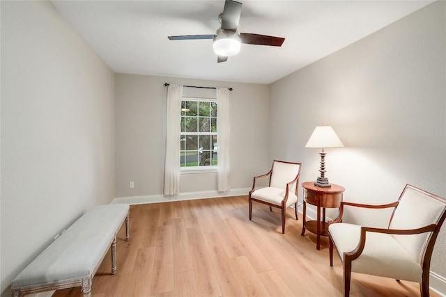 living area with baseboards, a ceiling fan, and light wood-style flooring