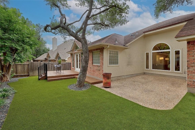 rear view of property featuring brick siding, fence, a yard, and a wooden deck