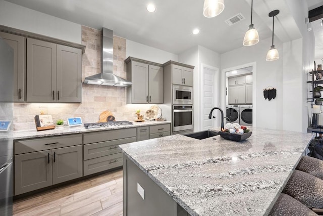 741 Faith Dr, Liberty Hill, TX 78642 - kitchen with gray cabinetry, appliances with stainless steel finishes, washing machine and dryer, wall chimney range hood, and a sink