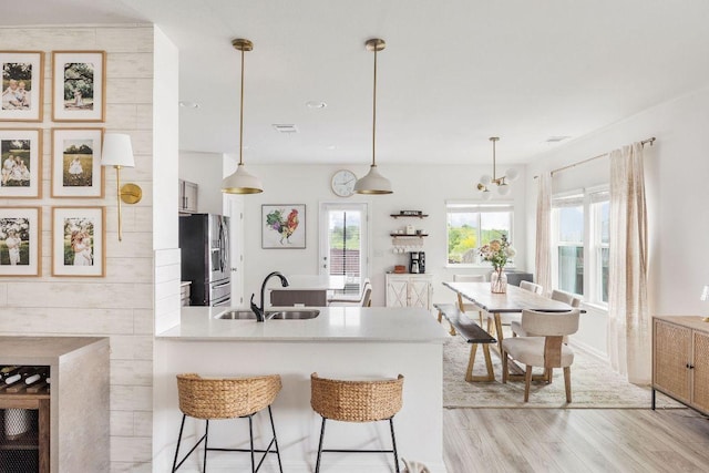 kitchen with a peninsula, a breakfast bar area, stainless steel refrigerator with ice dispenser, light wood-type flooring, and a sink