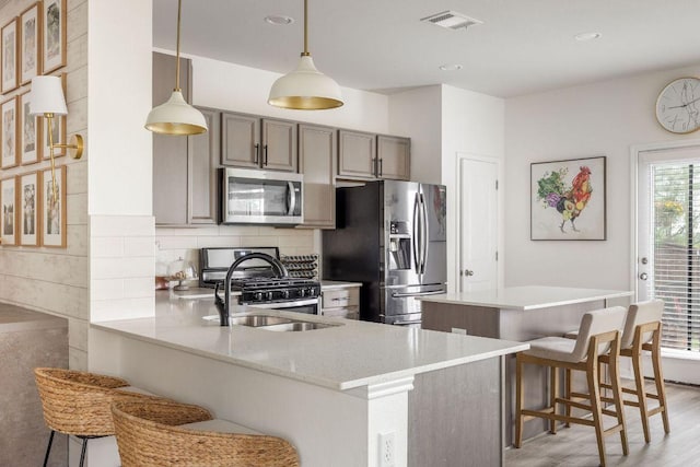 kitchen featuring stainless steel appliances, a peninsula, a kitchen bar, backsplash, and visible vents