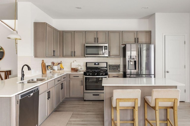 kitchen with a sink, light wood finished floors, light countertops, stainless steel appliances, and tasteful backsplash